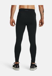 Leggings atletici neri con una vestibilità aderente, vita elastica e superficie liscia, abbinati a scarpe atletiche nere con accenti bianchi.
