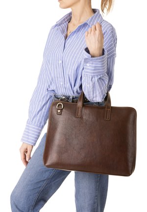 Borsa in pelle marrone con due manici corti, forma rettangolare, texture liscia e dettagli di cucitura visibili. Camicia a righe blu sullo sfondo.