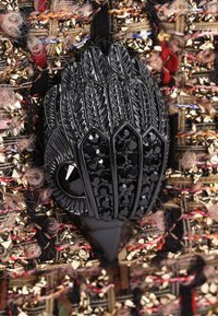 Spilla a forma di uccello nera con perline, con piume testurizzate su un tessuto intrecciato multicolore che presenta fili dorati e rosa.