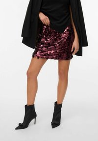 Krátká, těsně padnoucí sukně v burgundské barvě s velkými flitry. V kombinaci s černými kotníkovými botami se špičatými špičkami a mašlovými detaily.