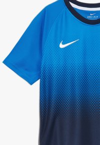 Camiseta deportiva azul Nike Dri-FIT de mangas cortas con un patrón de degradado de puntos que va del azul al azul oscuro.
