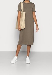 Khaki sukienka z krótkim rękawem, wykonana z miękkiego materiału, o prostym kroju. Połączona z beżową torbą na ramię i białymi sneakerami, na neutralnym tle.