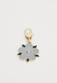 Porte-clés en forme de fleur dorée avec des pétales en paillettes argentées, des feuilles vert foncé, et un fermoir gravé du mot "Furla".