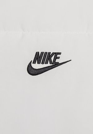 Sorte broderet "NIKE" logo på en hvid stofbaggrund, med et buet swoosh-design, der skaber en skarp kontrast.