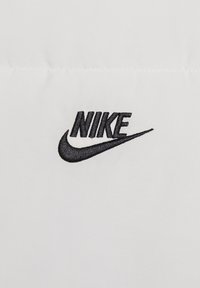 Biały materiał z wyraźnie wyhaftowanym czarnym logo Nike, prezentującym odważne litery i charakterystyczny wzór w kształcie znaku "swoosh".