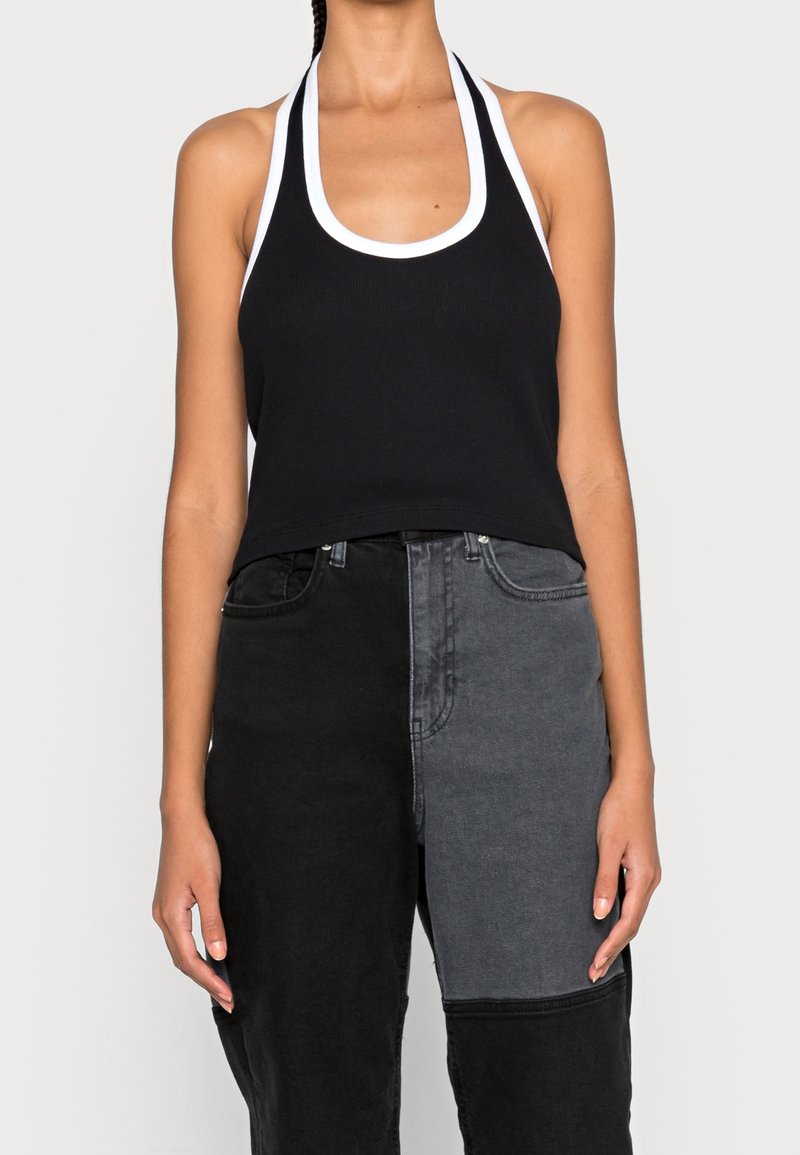 Top a halter nero a costine con rifiniture bianche, caratterizzato da un scollo a girocollo, design cropped e silhouette aderente. Modello abbinato a jeans in patchwork.