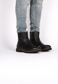 Stivali neri in pelle alla caviglia con finitura texturizzata, suola in gomma e cucitura a welt. Indossati con jeans in denim azzurro chiaro strappati.