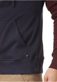 Sudadera con capucha de cuerpo azul marino oscuro y mangas burdeos. Presenta un bolsillo frontal y un pequeño logotipo negro cerca del dobladillo.
