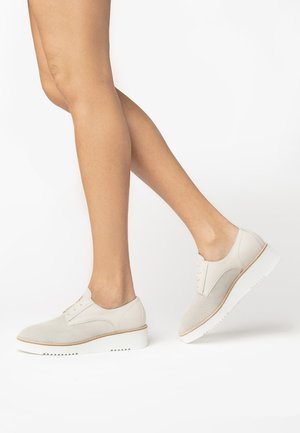 Scarpe beige chiare con lacci, con una tomaia in rete testurizzata, accenti in pelle liscia a contrasto e una suola bianca spessa con bordo seghettato.
