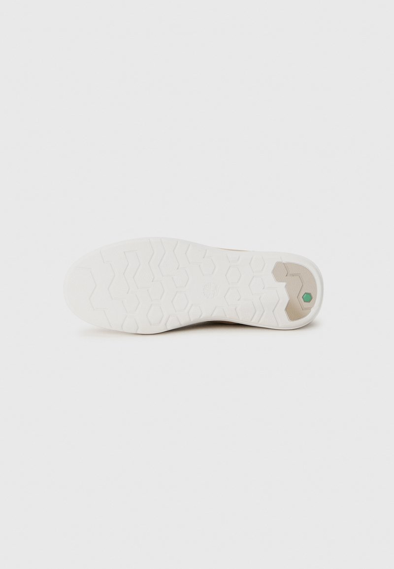 Zool van een beige schoen met een witte, textuur rubberen buitenzool met hexagonale looppatronen en een kleine groene hexagoon nabij de hiel.