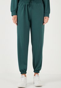 Pantaloni jogger color teal realizzati in tessuto morbido con vita e polsini elasticizzati. Presentano tasche laterali, vestibilità comoda e una superficie liscia.