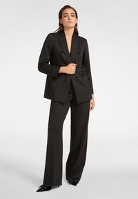 Schwarzer Nadelstreifenanzug mit einem doppeltknöpfigen Blazer und weiten Hosen, aus glattem Stoff, mit Reverskragen und schlanken Details.