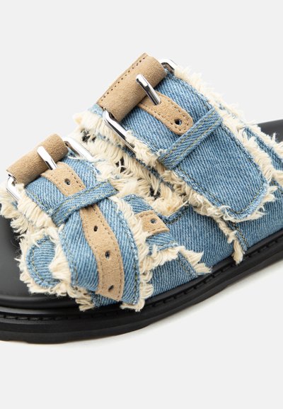 Ανοιχτό σανδάλι με μαύρη σόλα, διαθέτοντας μπλε τζιν λουράκια με ξεφτισμένες άκρες και ταμπά σουέτ κούμπωμα με πόρπη.