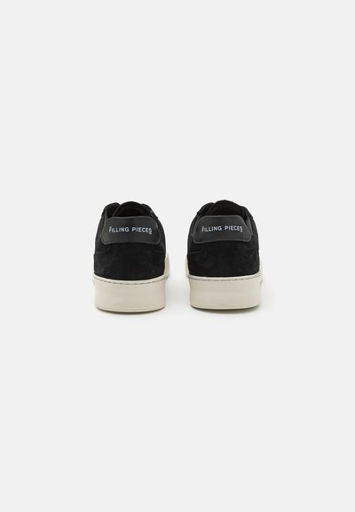 Black suede sneakers with a white sole, featuring a smooth back tab labeled "FILLING PIECES" in light blue. Simple, low-top design.