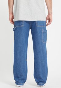 Jeans cargo en denim azul oscuro con un corte holgado. Cuenta con múltiples bolsillos, detalle del logo en amarillo y costuras en contraste.