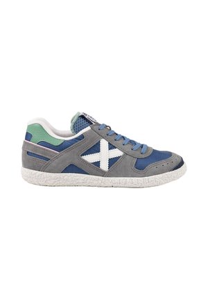 Zapatilla baja con malla azul y paneles de ante gris, suela blanca texturizada, detalle verde en el talón, cordones azules y logo blanco en forma de cruz en el lateral.