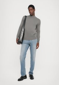 Pelēks garām piedurknēm turtlenecks, gaiši zili džinsi un melnas kurpes. Melna plecu soma. Vienkārša fona. Minimalistisks dizains.