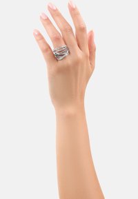 Anello d'argento con bande intrecciate, finitura lucida e gemme incastonate, esposto su una mano con unghie naturali.