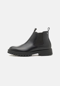 Bottines Chelsea en cuir noir avec panneau élastique sur le côté, languette de tirage et semelle en caoutchouc texturée. Design épuré, bout arrondi et détails de semelle.