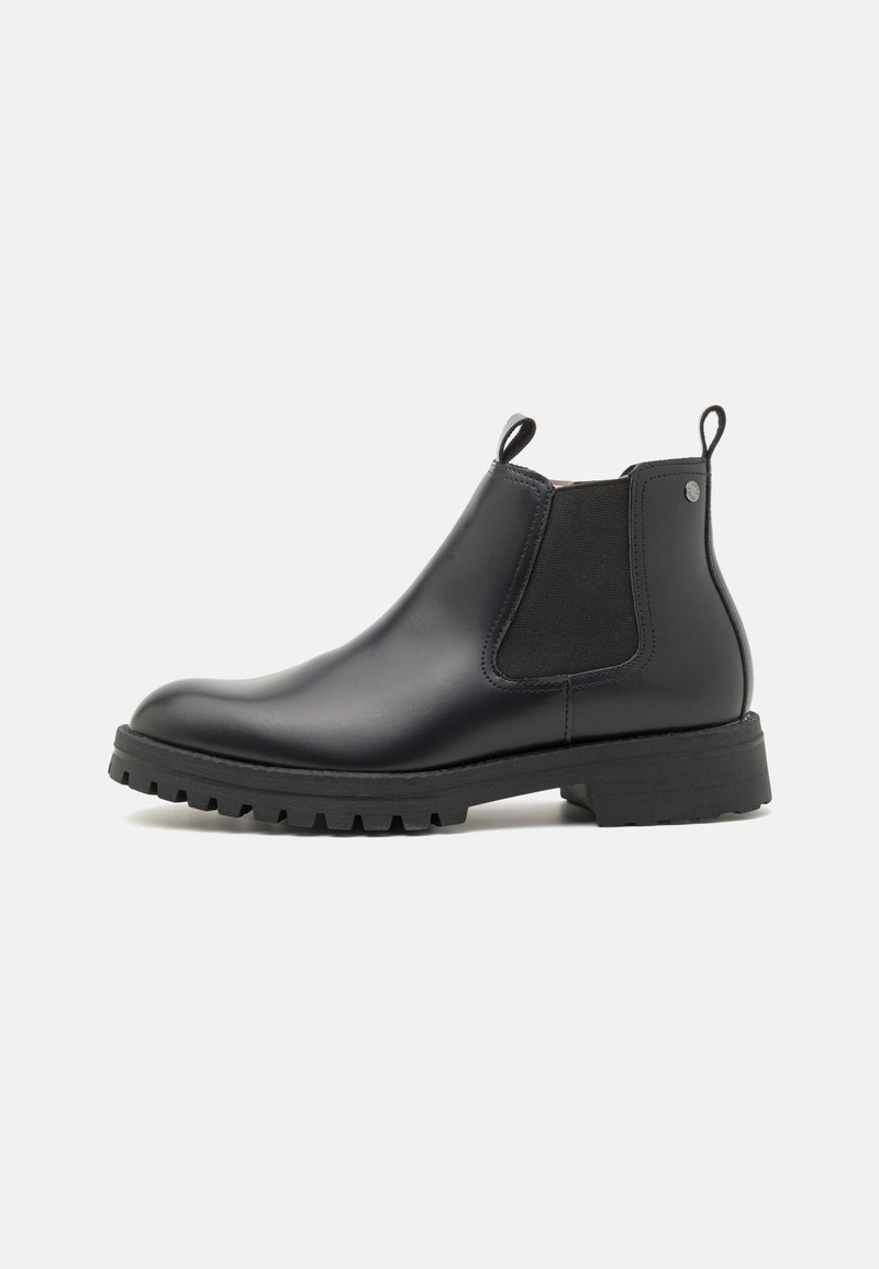 Bottines Chelsea en cuir noir avec panneau élastique sur le côté, languette de tirage et semelle en caoutchouc texturée. Design épuré, bout arrondi et détails de semelle.
