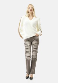 Wit gebreid sweater met V-hals en beige accenten, gecombineerd met versleten grijze jeans met meerdere scheuren. Zwarte hoge hakken.