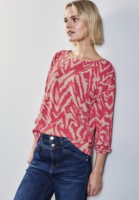 Roze en beige geblokt truitje met lange mouwen, gecombineerd met donkerblauwe strakke spijkerbroek met een gladde textuur en zichtbare hardware.