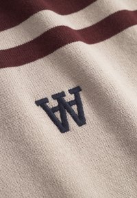 Beige strikket stof med to mørkerøde vandrette striber og broderede overlappende sorte bogstaver "W" og "A."
