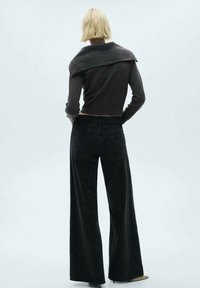 Mörkgrå kortad tröja med bred krage, ihopparad med högmidjade svarta vida jeans med en subtil mönstring.