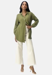 Groen textuur long-sleeve shirt met een knoopsluiting aan de voorkant, gecombineerd met witte wijde broek en sleehakken.