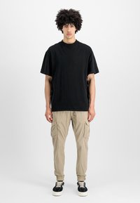 Črna bombažna majica s kratkimi rokavi v kombinaciji z bež cargo hlačami, ki imajo stranske žepe, elastične manšete ter črne čevlje z belimi podplati.