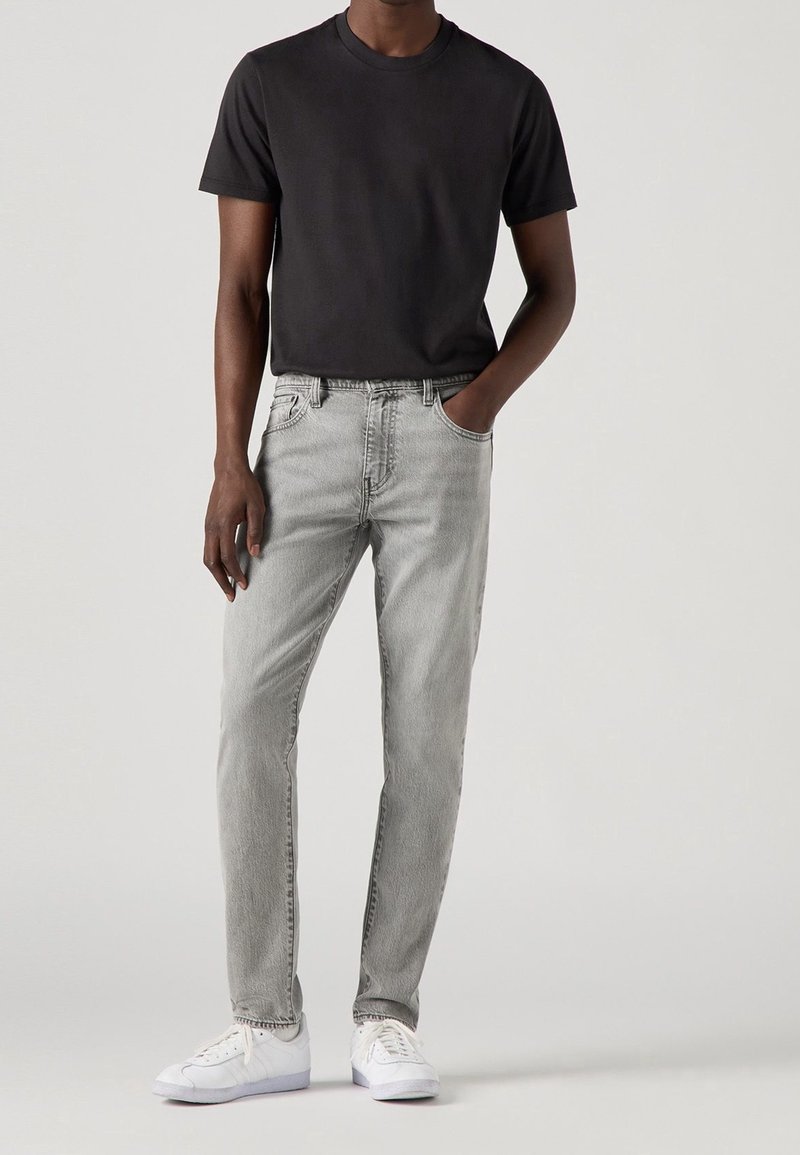 Camiseta negra de manga corta combinada con jeans de denim gris claro. Los jeans presentan un diseño clásico de cinco bolsillos y un ligero desvanecido. Zapatillas blancas complementan el look.