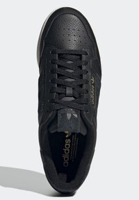 Černé kožené tenisky s texturovaným povrchem, které mají šněrování, perforace a zlaté logo. Gumová podešev s kontrastním bílým okrajem.