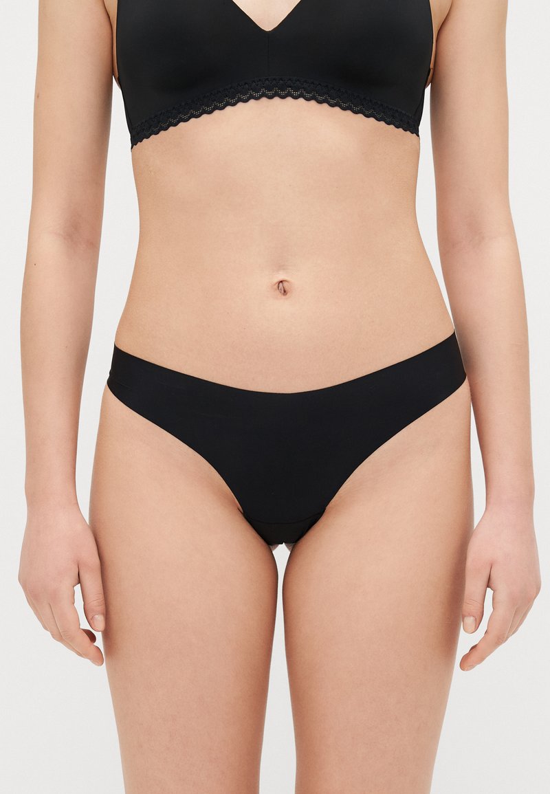 Black bikini briefs featuring a smooth, elastic material with a simple design and low-rise cut, creating minimal coverage.