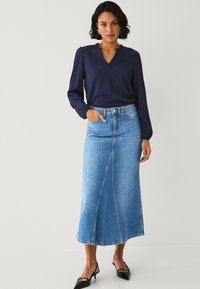 Blusa blu navy con scollatura a onda abbinata a una gonna lunga in denim azzurro chiaro con cucitura frontale. Tacchi neri a punta completano il look.