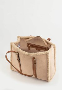 Bolso tote de piel sintética tipo shearling en color crema con detalles de cuero marrón, bolsillo interior con cremallera y dos correas para el hombro. Diseño abierto con interior espacioso.