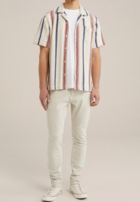 Kortärmad, knappupp skjorta med röda, blå och gräddfärgade vertikala ränder, texturerat tyg, ficka på vänster bröst, bärs över en vit t-shirt.