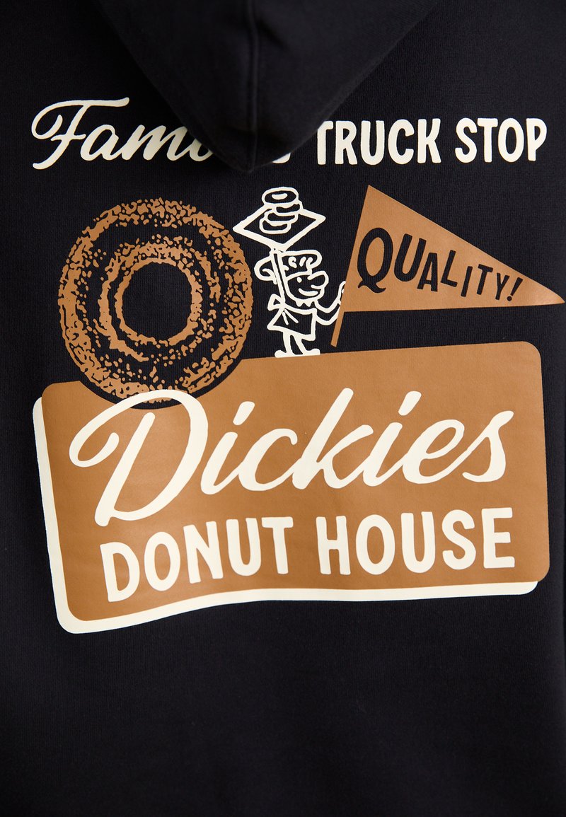 Felpa nera con grafica che presenta una ciambella, il testo "Dickies Donut House" e un personaggio dei cartoni animati che tiene un vassoio, accentuato in bianco e marrone.