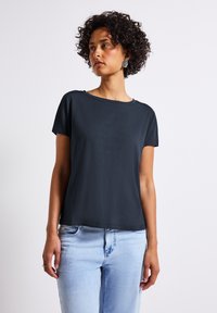 T-shirt à manches courtes bleu foncé avec une coupe décontractée, texture lisse et encolure ronde, associé à un jean bleu clair.