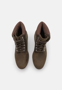 Stivali alla caviglia in pelle marrone con colletto imbottito, occhielli in metallo e lacci. Presentano una suola robusta e una superficie liscia.
