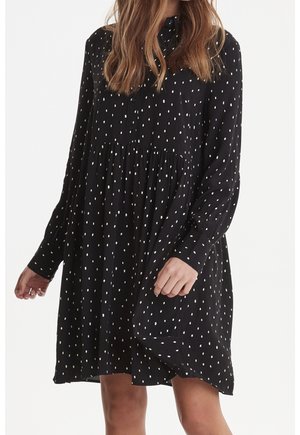 Robe longue noire à manches longues avec un col boutonné, ornée de pois blancs, taille froncée et coupe ample. Texture de tissu douce.