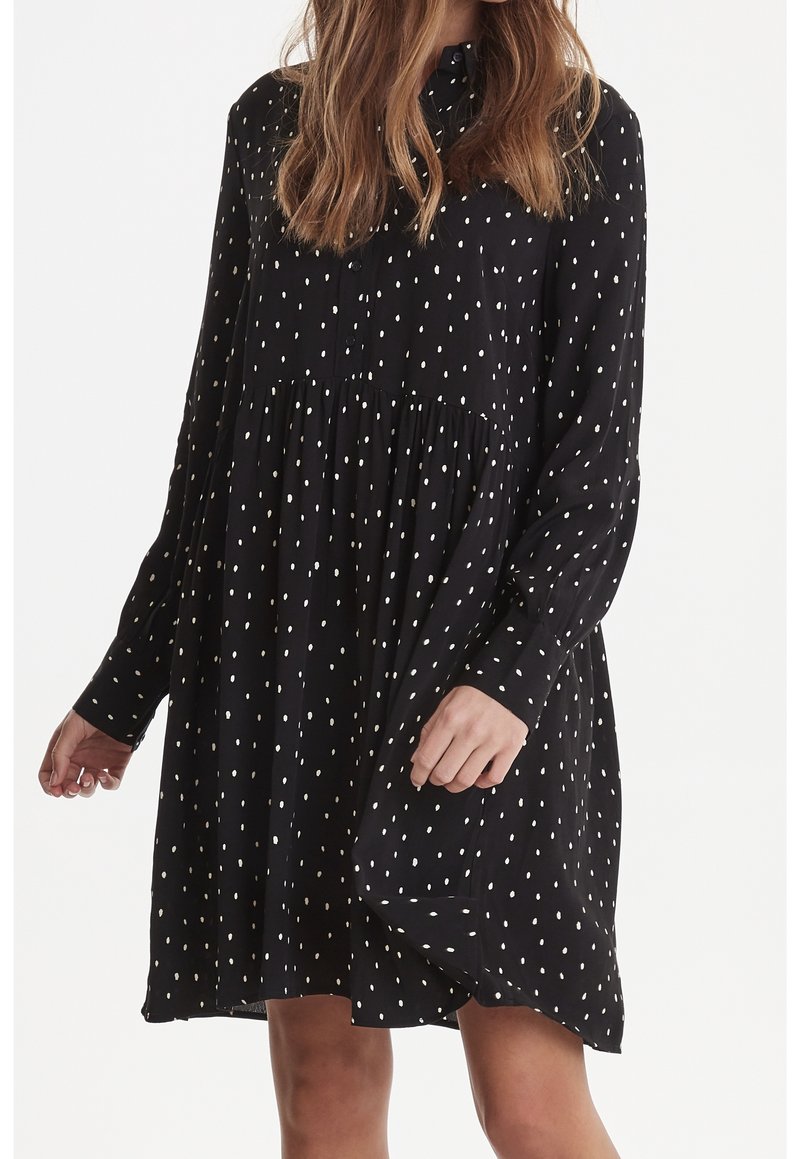 Abito nero a maniche lunghe con colletto button-down, caratterizzato da pois bianchi, vita arricciata e vestibilità ampia. Texture del tessuto morbida.