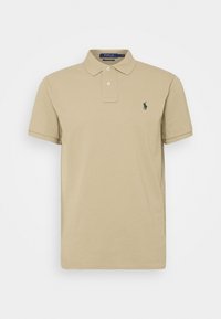 Beige bomullspiké med kort ärm, standardkrage, två knappar och en grön broderad logotyp på vänstra bröstet.