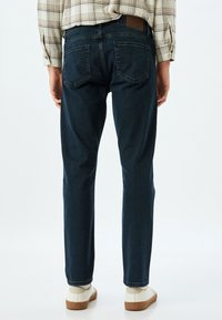 Jeans de color azul oscuro en corte recto, con una cintura de altura media, bolsillos traseros y una etiqueta de cuero en la cinturilla. Llevados con zapatillas blancas.