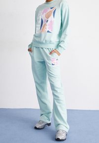 Completo felpa e pantaloni della tuta color teal chiaro realizzato in materiale morbido, con vivaci grafiche colorate e una cintura elastica con tasche.