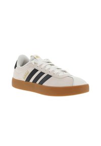 Zapatillas con parte superior de lona color crema claro, rayas de piel negra y suela de goma. Presenta cordones planos blancos y un acento de logotipo dorado.