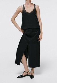 Completo in satin nero con top senza maniche con dettagli in pizzo e pantaloni a gamba larga, alla caviglia, con spacco laterale. Ballerine a punta completano il look.