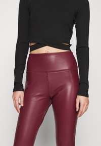 Svart ribbad långärmad topp med en croppad design, kombinerad med vinröda leggings i konstl äder med hög midja och en slät yta.