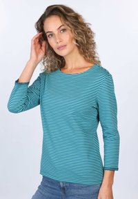 T-Shirt mit langen Ärmeln in Teal und Blau mit einem Bootsausschnitt, gewellten Ärmelkanten und weichem Stoff, kombiniert mit Jeans.