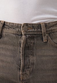 Mørk grå denimjeans med synlig søm og metallknap-lukking, med en klassisk fem-lomme design og en litt falmet tekstur.