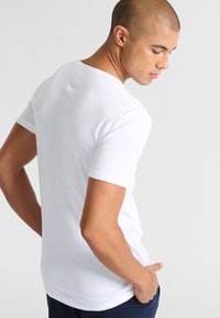 Kortärmad vit t-shirt gjord av mjuk bomull. En åtsittande design med klassisk rund hals och enkel tyg, utan mönster eller detaljer.